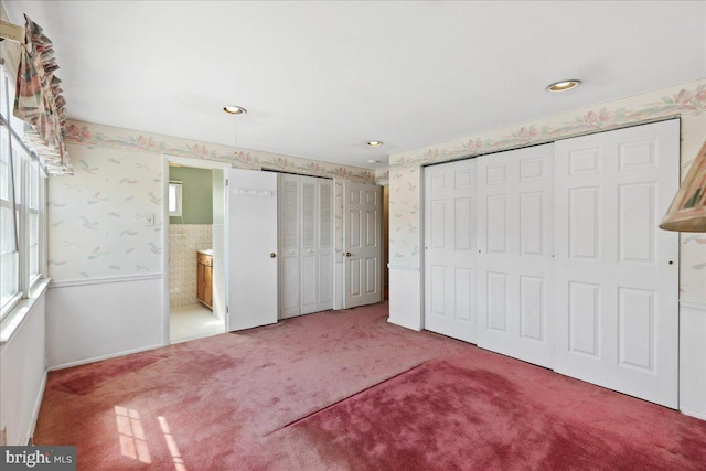 unfurnished bedroom with wallpapered walls, ensuite bath, multiple closets, and carpet floors