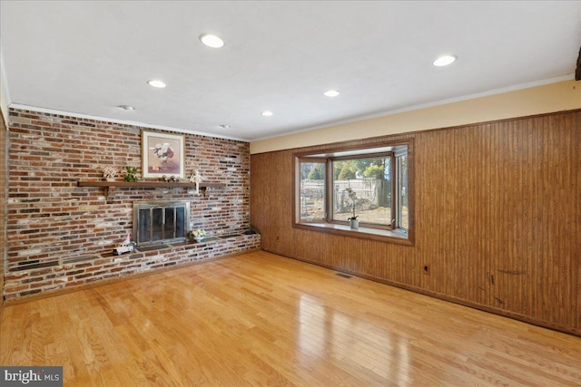 unfurnished living room with a brick fireplace, wood finished floors, brick wall, and ornamental molding