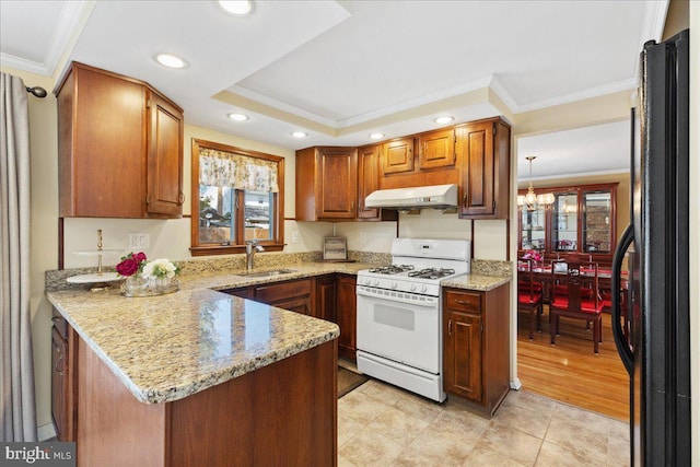 kitchen featuring under cabinet range hood, white gas range, a peninsula, freestanding refrigerator, and a sink