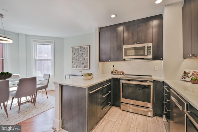 kitchen featuring dark brown cabinets, light countertops, light wood-style flooring, appliances with stainless steel finishes, and a peninsula