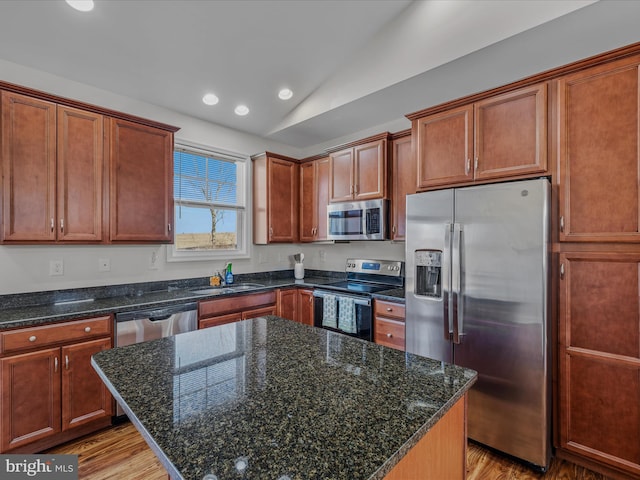 kitchen with a sink, stainless steel appliances, light wood-style flooring, and vaulted ceiling