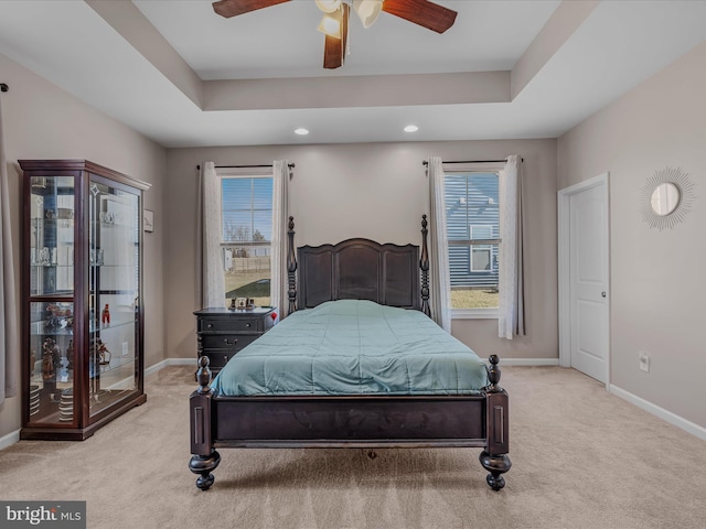 bedroom with a raised ceiling, light colored carpet, baseboards, and ceiling fan