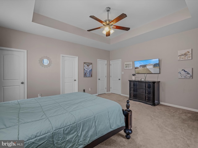 bedroom featuring light colored carpet, baseboards, a tray ceiling, and ceiling fan