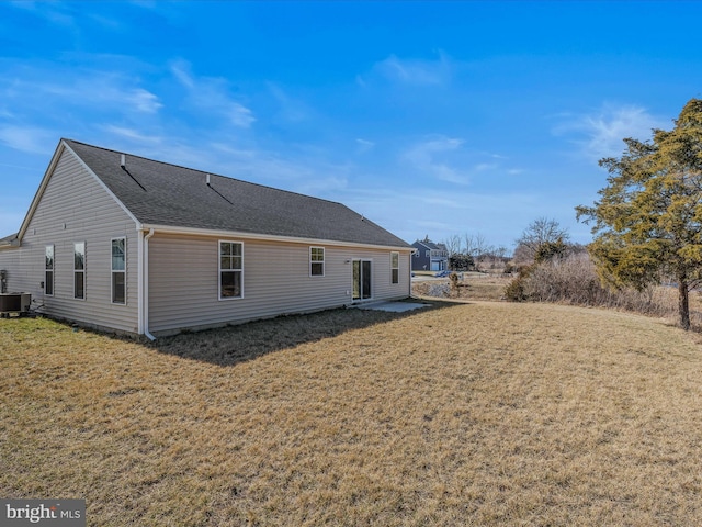 rear view of house featuring a lawn, central AC, and roof with shingles