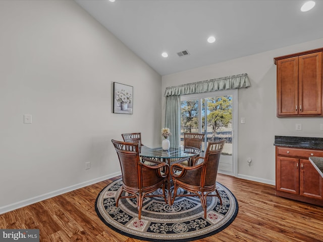 dining area with visible vents, baseboards, wood finished floors, and vaulted ceiling