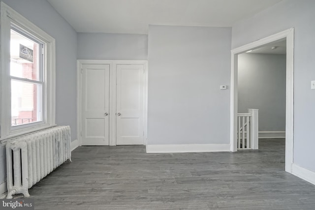 unfurnished room featuring radiator heating unit, wood finished floors, and baseboards