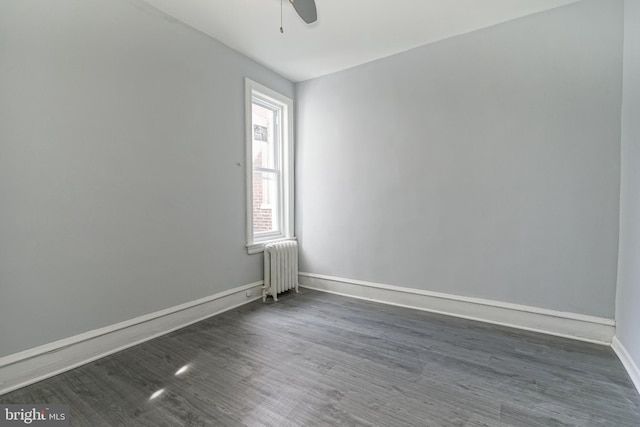 spare room featuring baseboards, a ceiling fan, dark wood-style flooring, and radiator heating unit