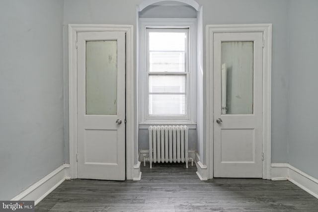 interior space featuring arched walkways, radiator, baseboards, and wood finished floors