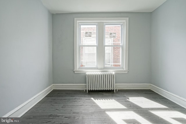 empty room with radiator heating unit, wood finished floors, and baseboards