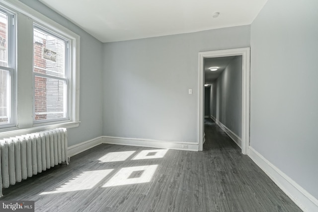 empty room with radiator heating unit, baseboards, and wood finished floors