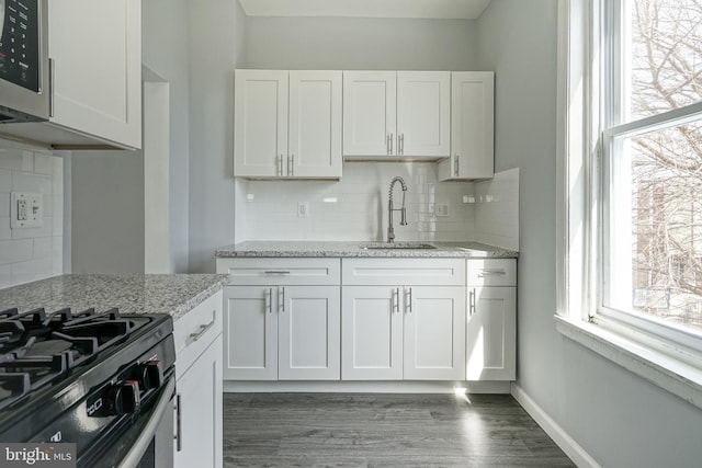 kitchen with light stone counters, baseboards, a sink, white cabinets, and stainless steel microwave