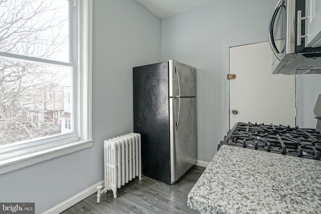 kitchen with stainless steel appliances, plenty of natural light, wood finished floors, and radiator heating unit