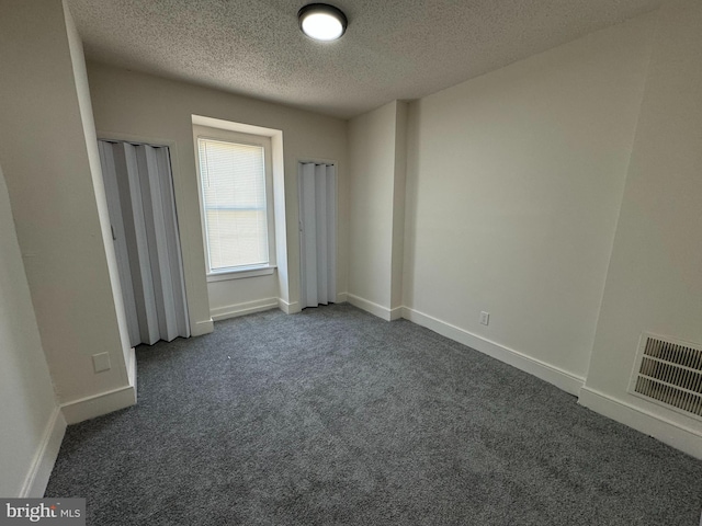 unfurnished bedroom with visible vents, a textured ceiling, baseboards, and dark colored carpet