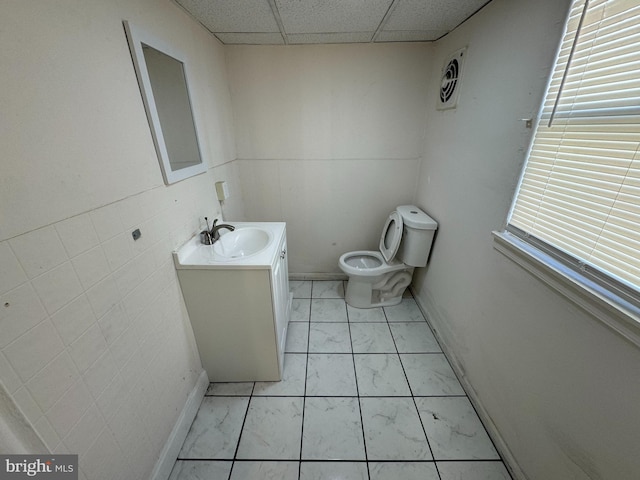 bathroom featuring toilet, marble finish floor, a drop ceiling, baseboards, and vanity