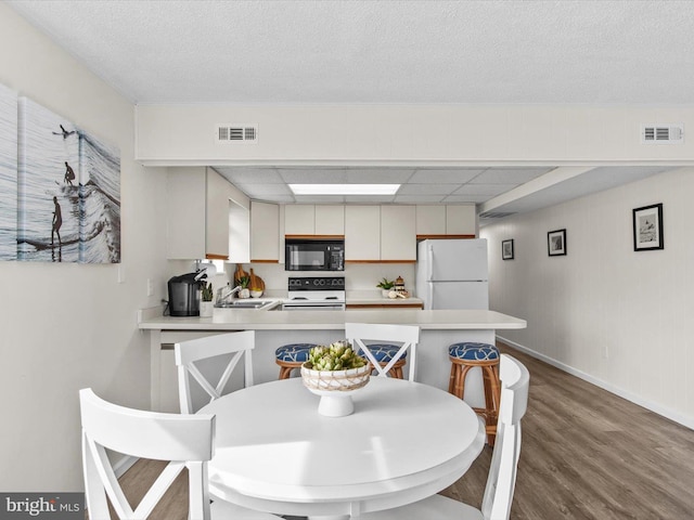 dining area featuring visible vents, a paneled ceiling, baseboards, and wood finished floors