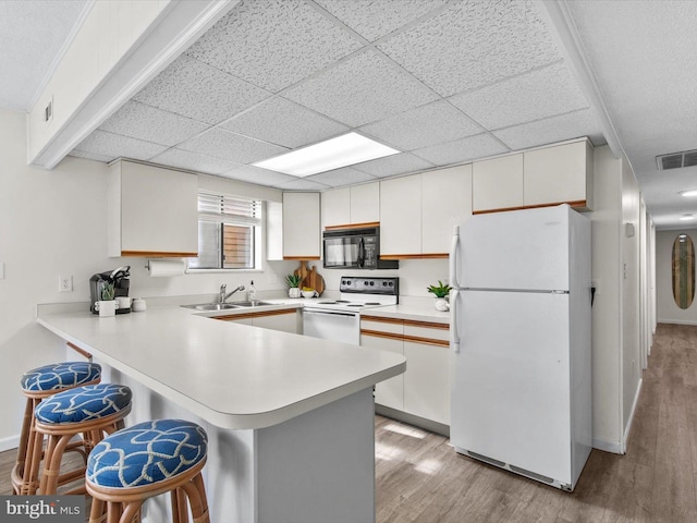 kitchen with white appliances, visible vents, a peninsula, a sink, and light countertops