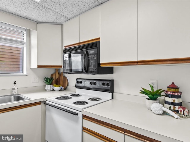 kitchen with white electric stove, light countertops, a paneled ceiling, black microwave, and white cabinetry