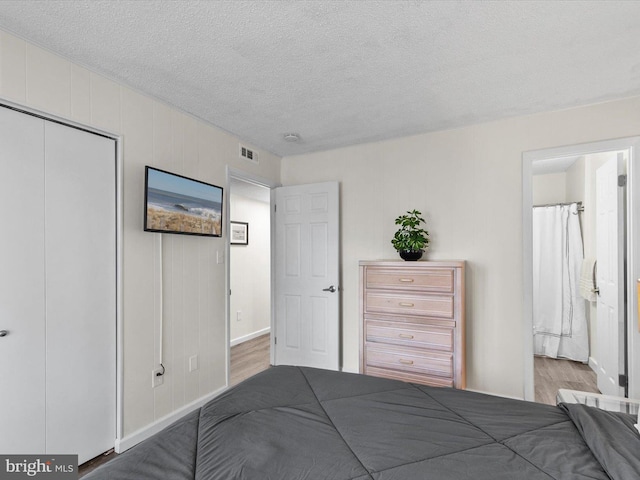 bedroom featuring visible vents, ensuite bathroom, wood finished floors, a closet, and a textured ceiling