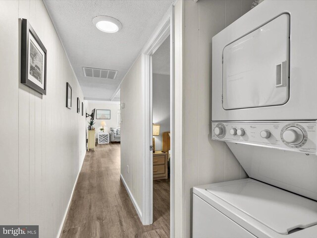 laundry area with wood finished floors, visible vents, laundry area, stacked washer and dryer, and a textured ceiling