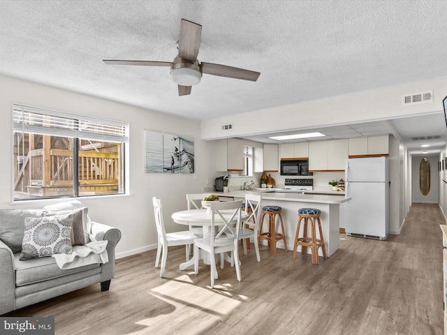 dining area featuring visible vents, a textured ceiling, light wood finished floors, baseboards, and ceiling fan