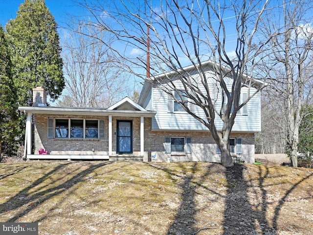 tri-level home featuring brick siding, a porch, and a chimney