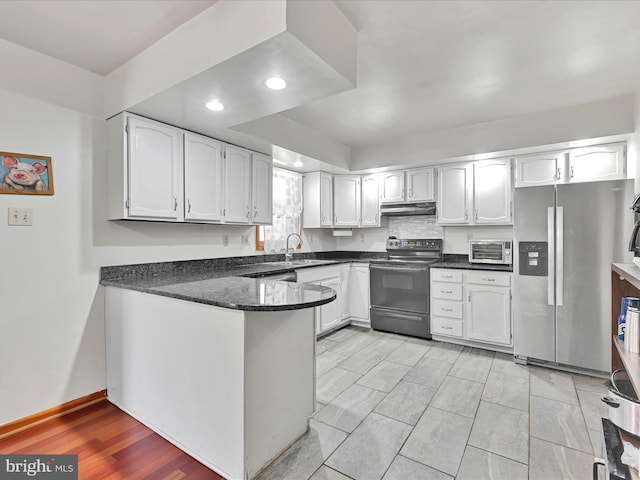 kitchen featuring black range with electric stovetop, under cabinet range hood, a peninsula, stainless steel fridge, and a sink