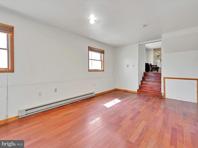 empty room with hardwood / wood-style flooring, stairway, baseboards, and a baseboard radiator