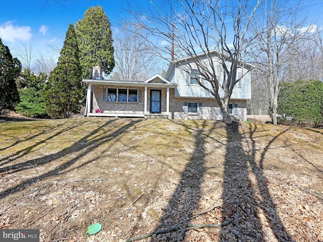 split level home with brick siding, covered porch, a chimney, and a front lawn