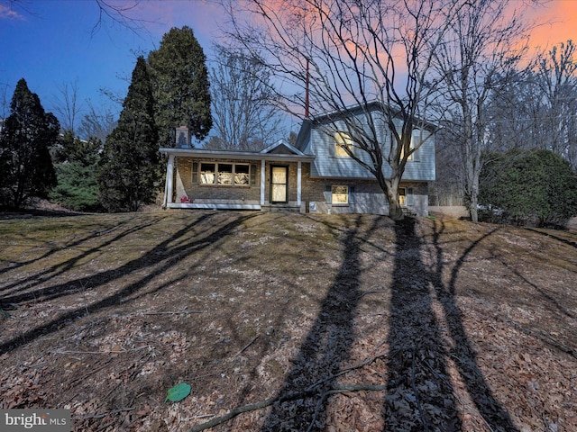 split level home with brick siding, a porch, and a chimney