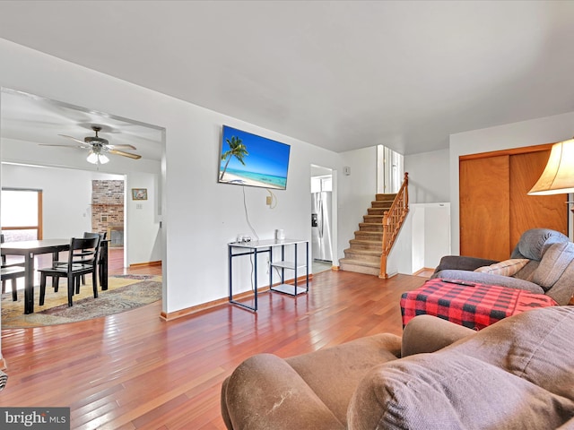 living room with baseboards, stairway, a fireplace, hardwood / wood-style flooring, and a ceiling fan