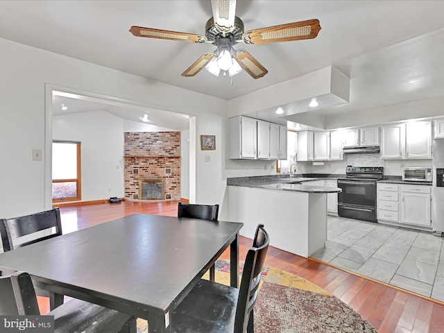 dining room featuring a toaster, vaulted ceiling, light wood-style flooring, a fireplace, and a ceiling fan