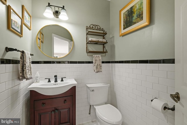 half bathroom with vanity, tile walls, toilet, and a wainscoted wall