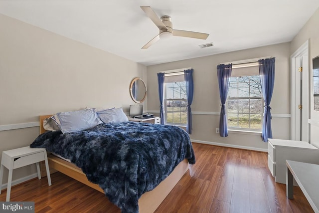 bedroom with ceiling fan, visible vents, baseboards, and wood finished floors