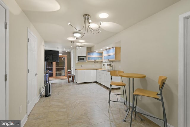 kitchen with stainless steel microwave, baseboards, a notable chandelier, white cabinetry, and open shelves