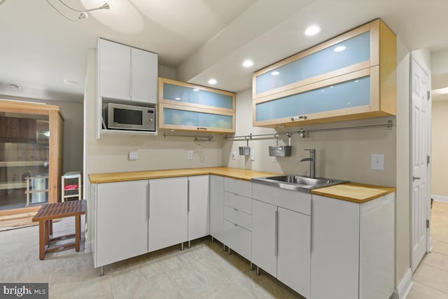 kitchen with stainless steel microwave, butcher block counters, recessed lighting, white cabinetry, and a sink