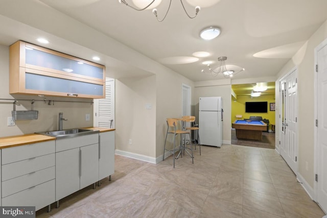 kitchen with baseboards, butcher block counters, freestanding refrigerator, billiards, and a sink