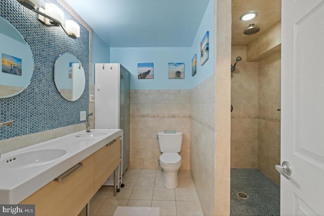 bathroom with tiled shower, a sink, tile walls, toilet, and tile patterned floors