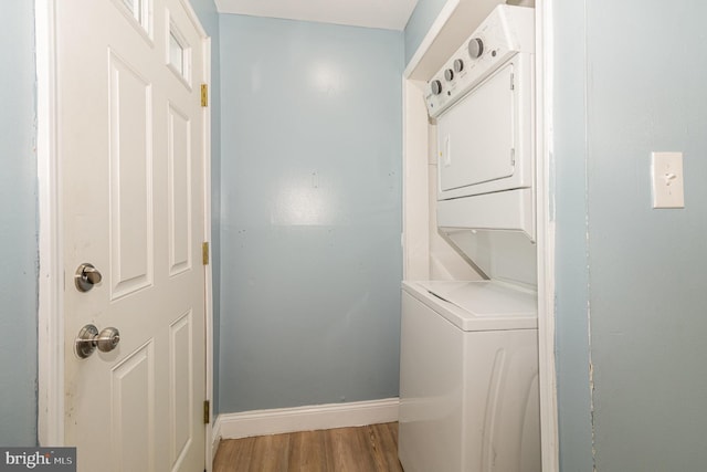 clothes washing area featuring light wood finished floors, laundry area, stacked washer and clothes dryer, and baseboards