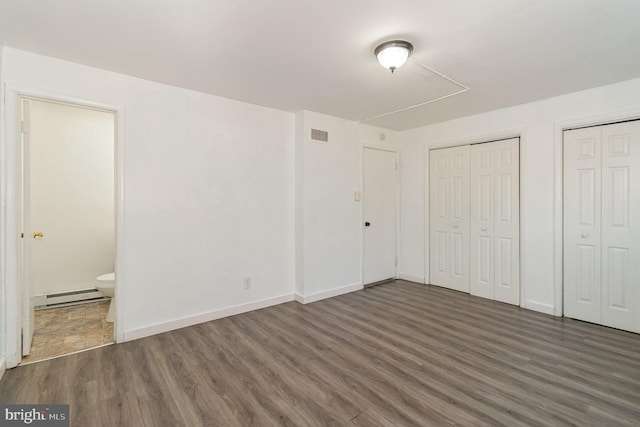 unfurnished bedroom featuring a baseboard heating unit, wood finished floors, multiple closets, and ensuite bathroom