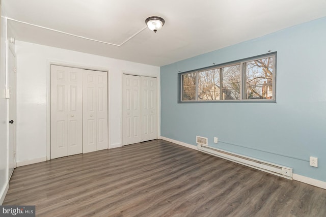 unfurnished bedroom with a baseboard radiator, multiple closets, baseboards, and wood finished floors