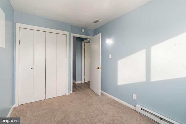 unfurnished bedroom with visible vents, a baseboard heating unit, baseboards, carpet flooring, and a closet