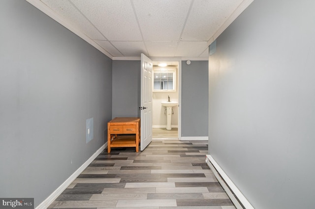 hall with a sink, a baseboard heating unit, wood finished floors, baseboards, and a paneled ceiling