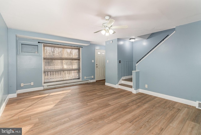 unfurnished living room with stairway, a baseboard heating unit, and wood finished floors