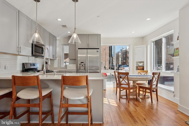 kitchen featuring light wood-style flooring, gray cabinets, a peninsula, appliances with stainless steel finishes, and decorative backsplash