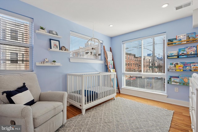 bedroom featuring recessed lighting, visible vents, a nursery area, and wood finished floors