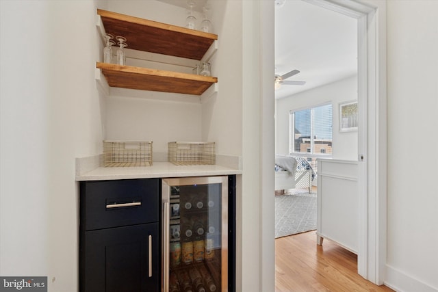 bar featuring ceiling fan, light wood-type flooring, baseboards, and beverage cooler