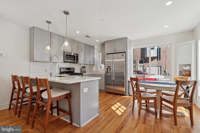 kitchen featuring decorative backsplash, appliances with stainless steel finishes, a peninsula, and gray cabinetry