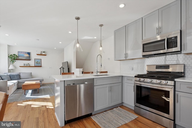 kitchen with gray cabinetry, open floor plan, a peninsula, stainless steel appliances, and a sink