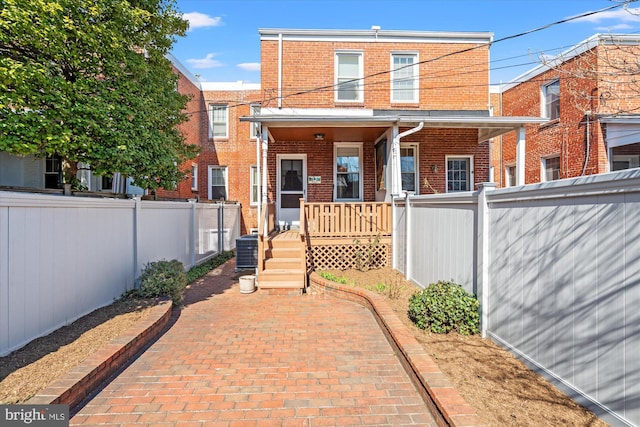 back of house with central AC unit, brick siding, covered porch, and fence private yard