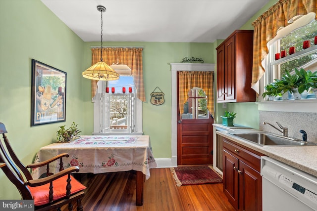 kitchen with wood finished floors, white dishwasher, a sink, light countertops, and pendant lighting